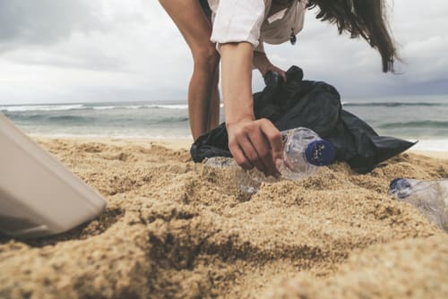 Woman picks up plastic litter off beach